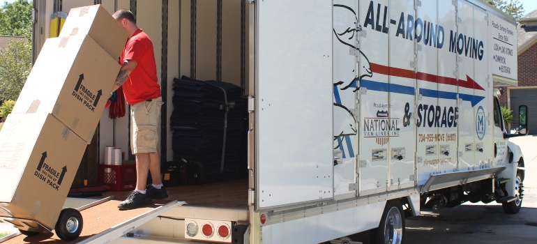 Warren MI movers unload a large cardboard box from the back of a moving truck