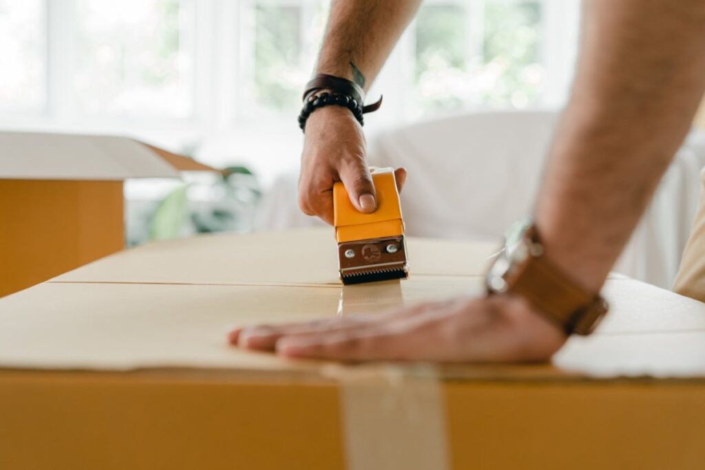 A person using a tape dispenser to seal a large cardboard box