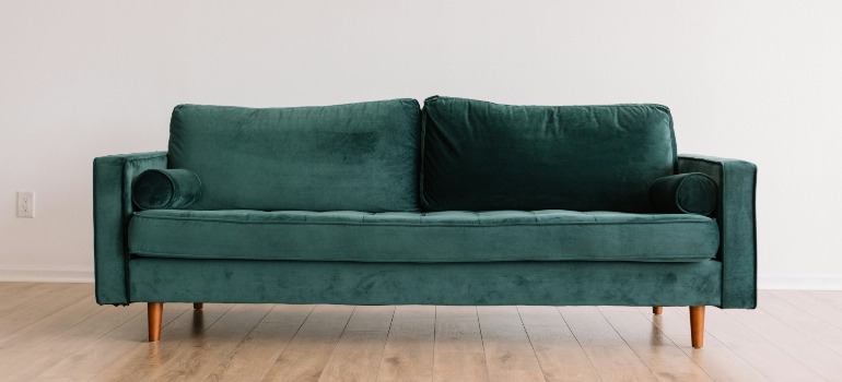 A stylish green velvet couch with wooden legs