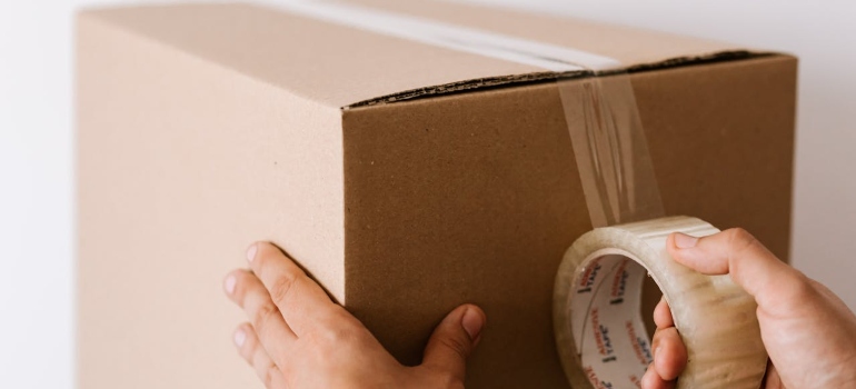 A person sealing a cardboard box with clear packing tape, preparing it for shipping or storage.
