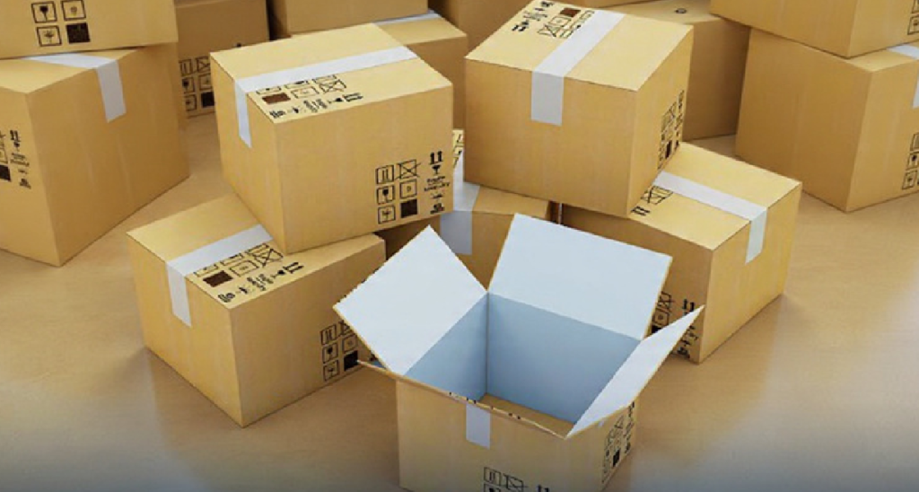 Stack of cardboard shipping boxes sealed with white tape, one open box showing its empty interior, with printed handling symbols like fragile, keep dry, and this side up on the sides.