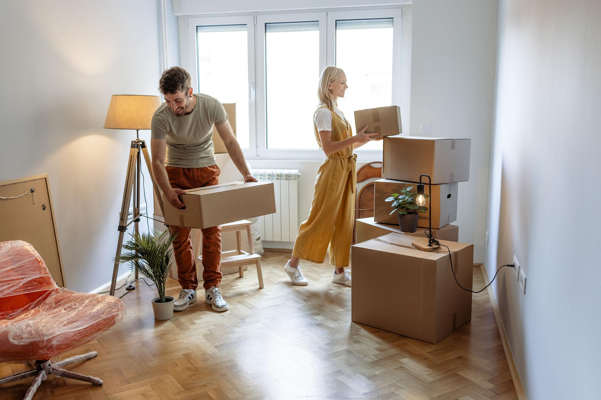 Couple unpacking cardboard boxes and organizing belongings inside a new home during a residential move.